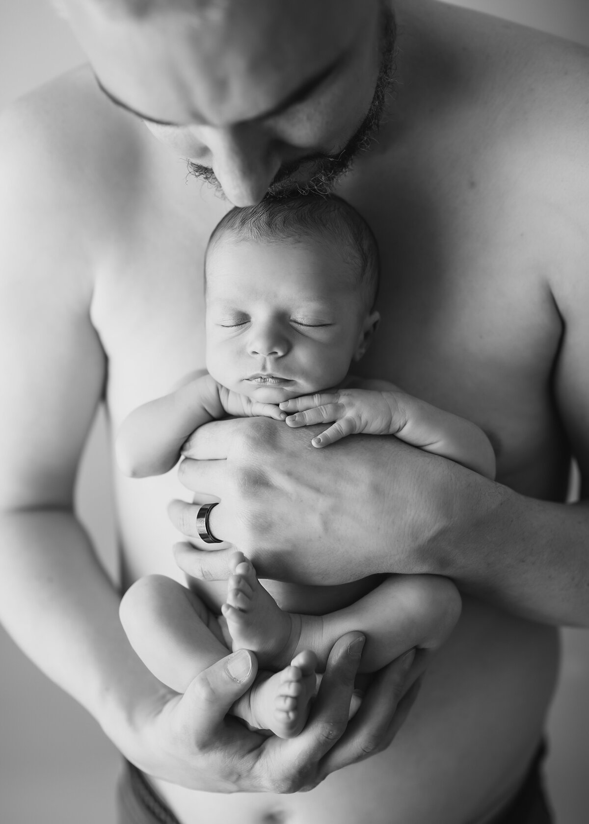 Black & white studio newborn pictures Dad kisses baby on top of head