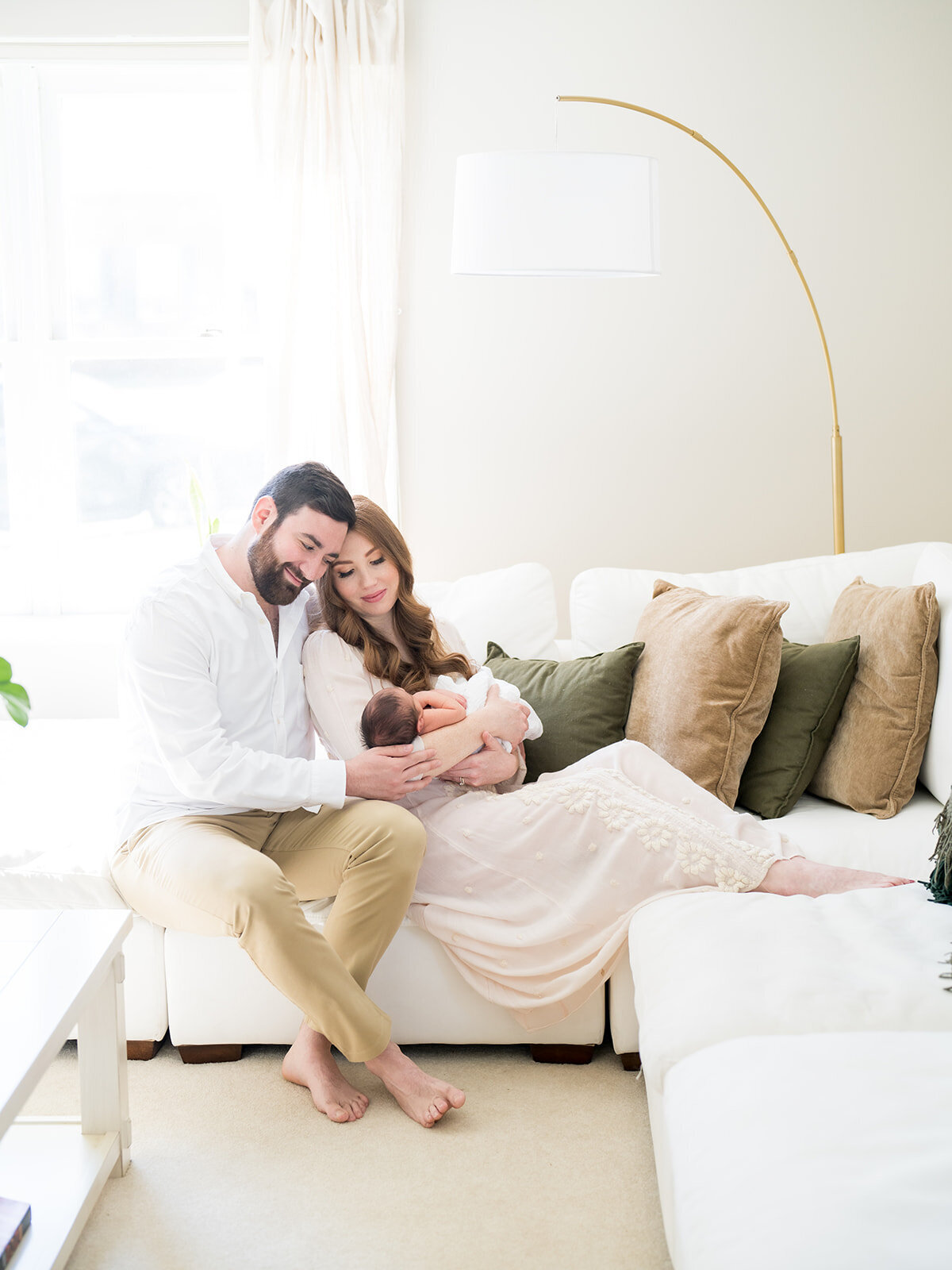 Mother sits on couch holding newborn baby boy while leaning into her husband during their Arnold newborn session.