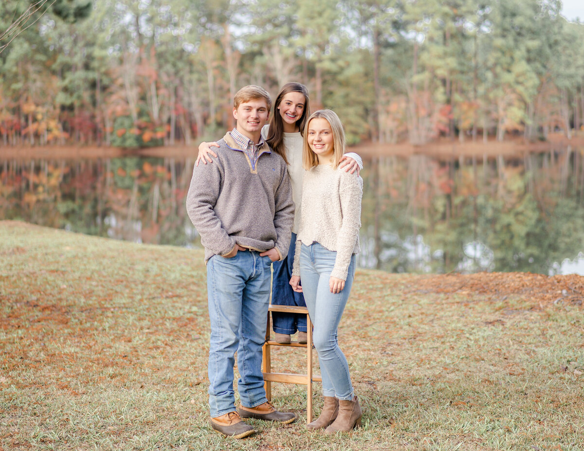 Teenage brother with his sisters standing on ladder at the pond at their family home