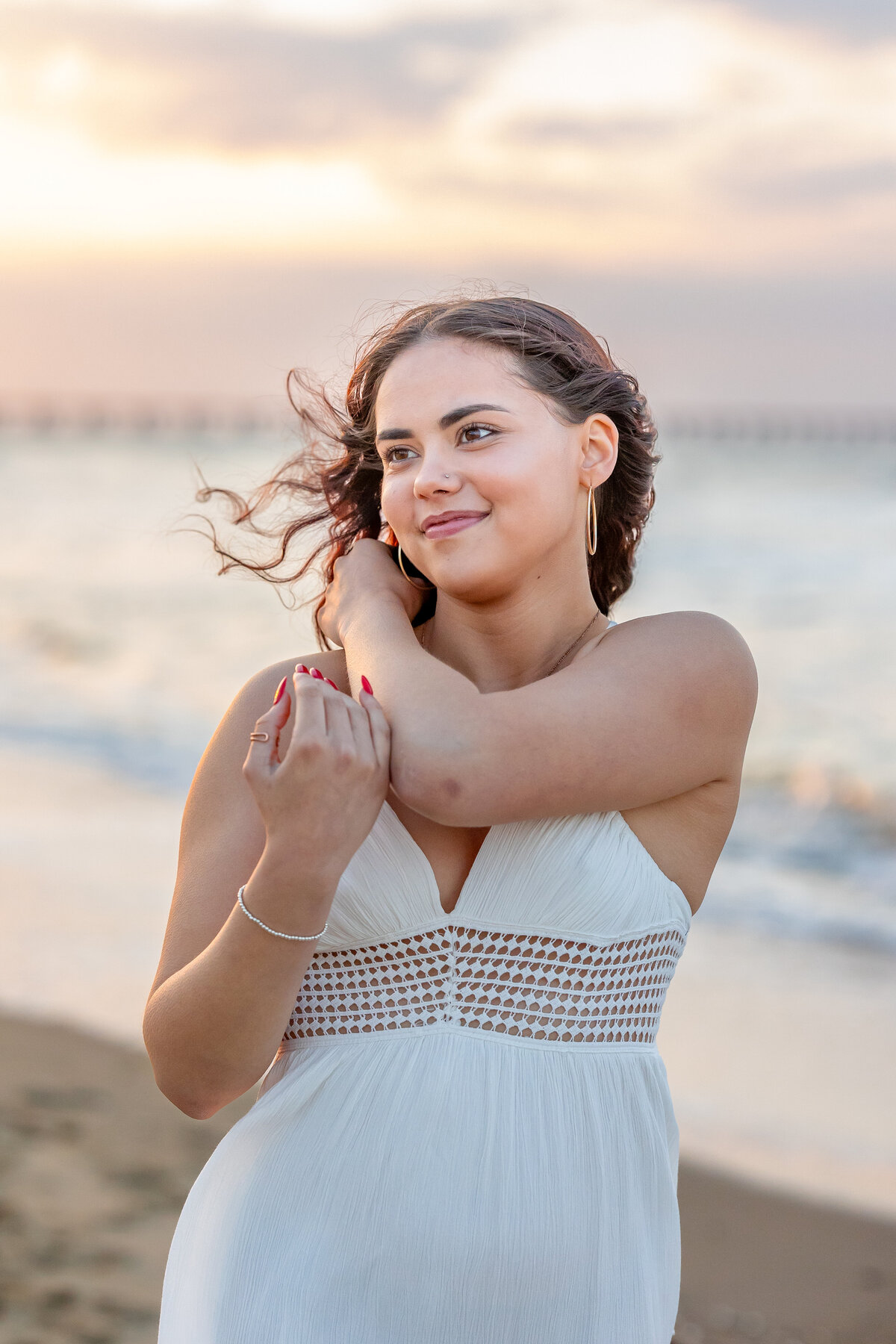 High school senior stands confidently at the shoreline in Coastal Virginia, the ocean breeze catching her curls as golden light dances across the waves behind her- captured by Brooke Tucker