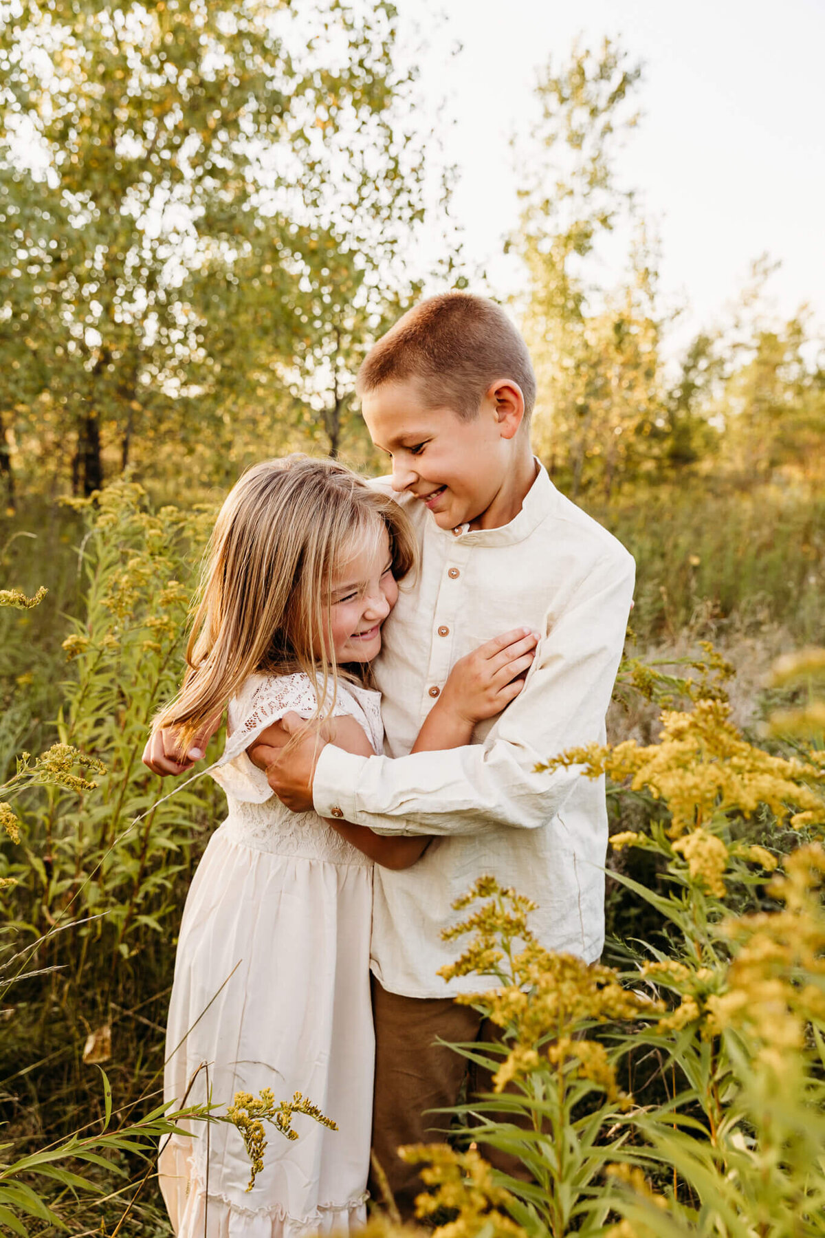 brother and sister in white clothing tickling each other in goldenrod by Ashley Kalbus