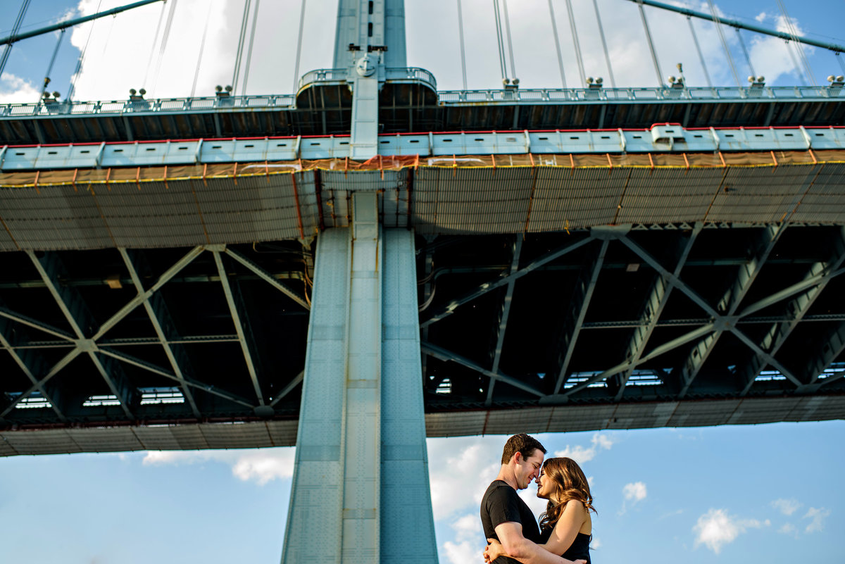 The ben franklin bridge frames a happy couple against the blue sky.