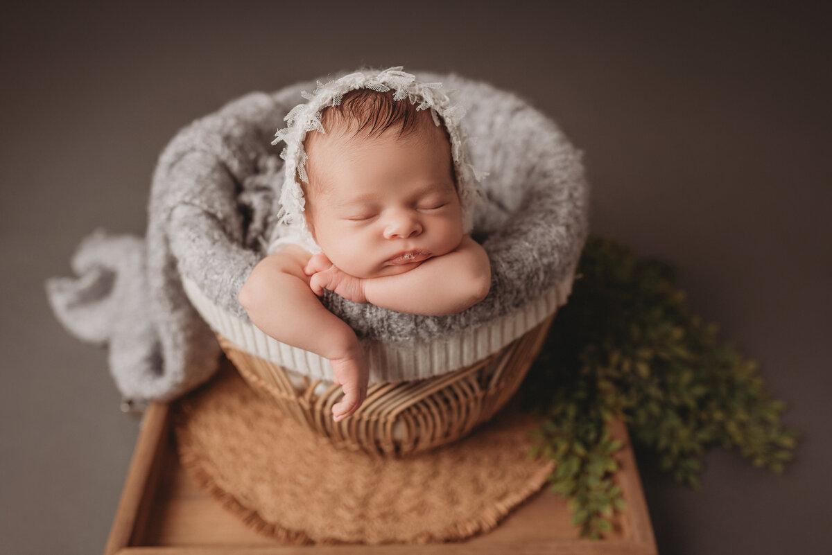 baby girl at her newborn portrait session at Marietta, GA newborn photography studio sleeping in basket and curled up while posing for her newborn portrait
