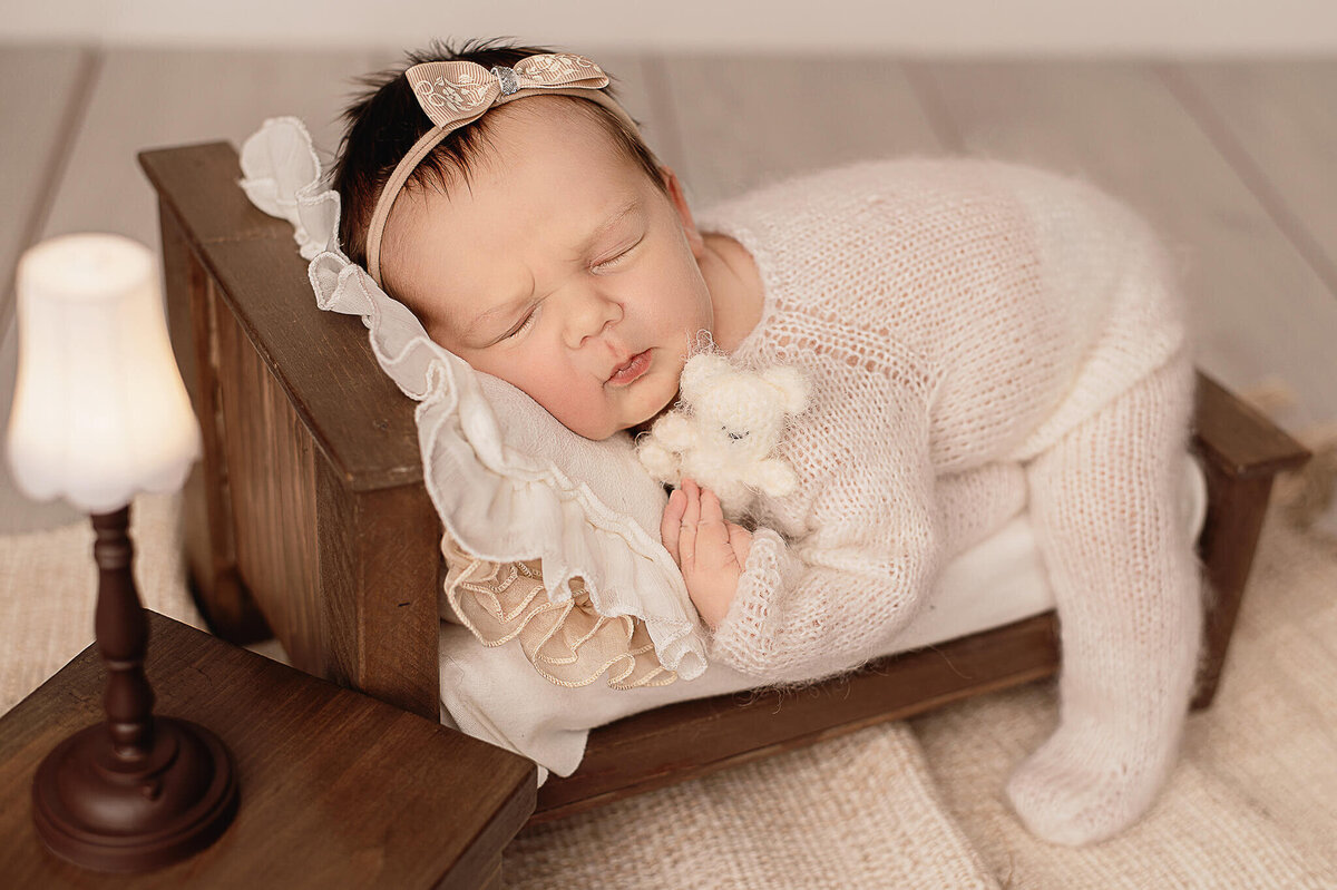 Baby girl sleeping with a teddy on a little prop bed at her newborn session.