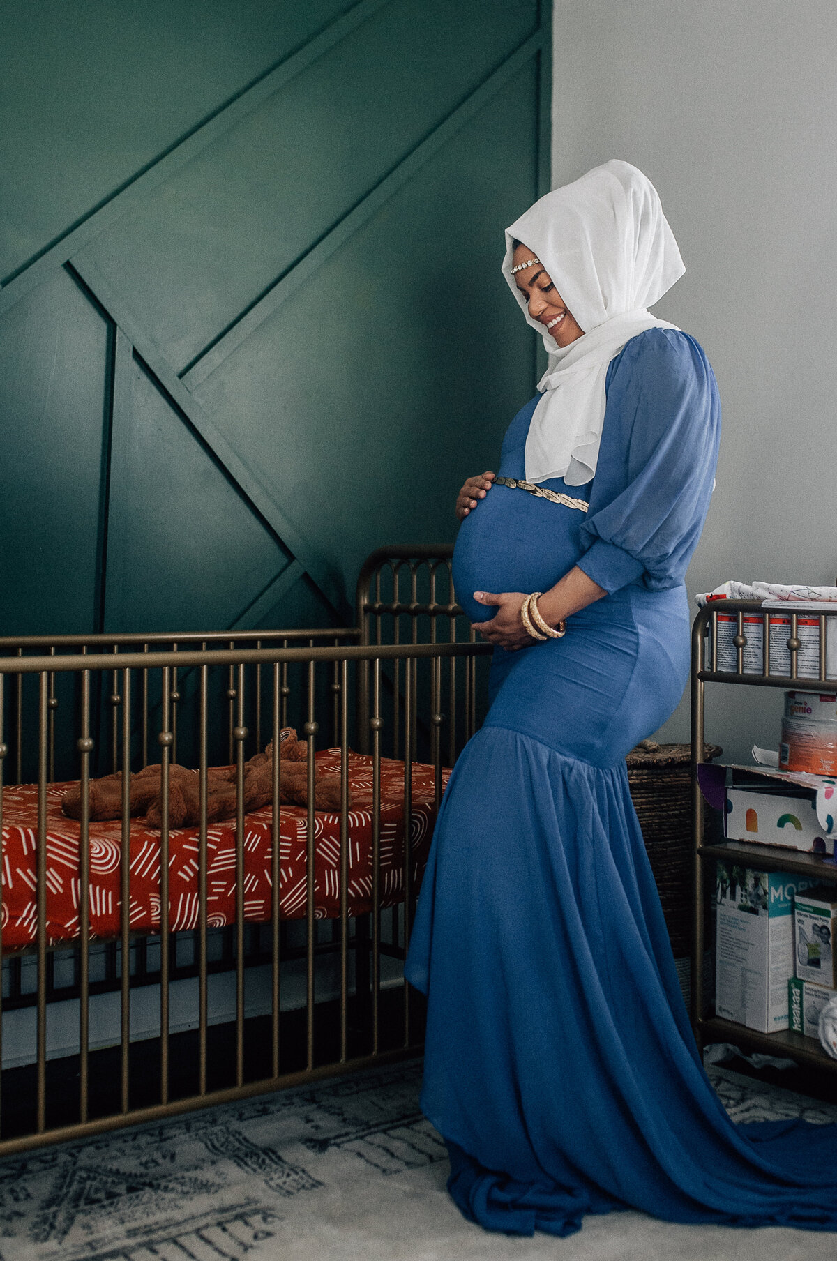 Maternity photoshoot with woman standing next to a crib.