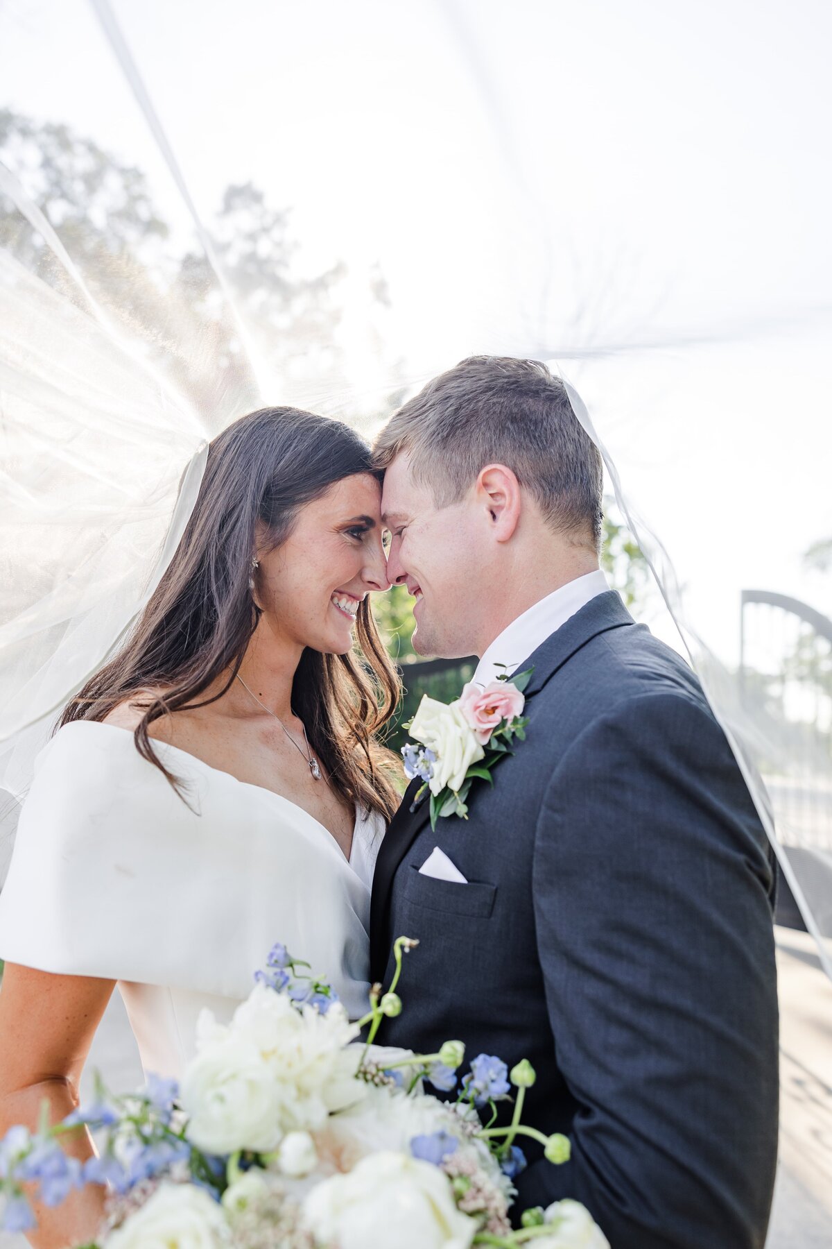 Newlyweds snuggle under the veil touching foreheads and holding white and blue veil