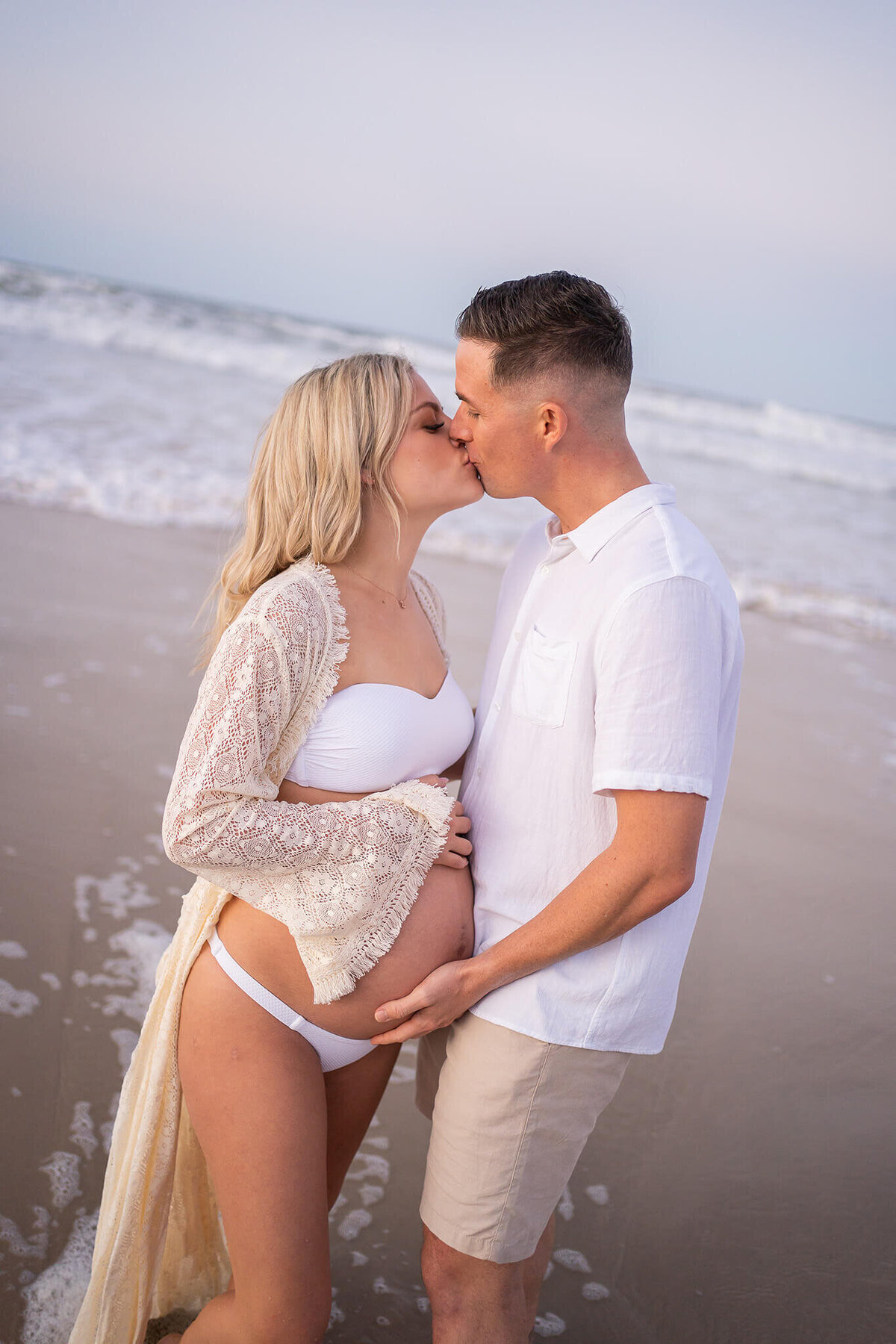 couple kissing on the beach holding belly bump during maternity photo session in Gold Coast