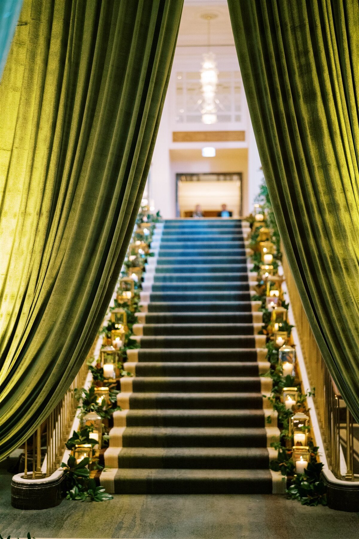 A picture of the staircase lined with candles beyond green drapes. 