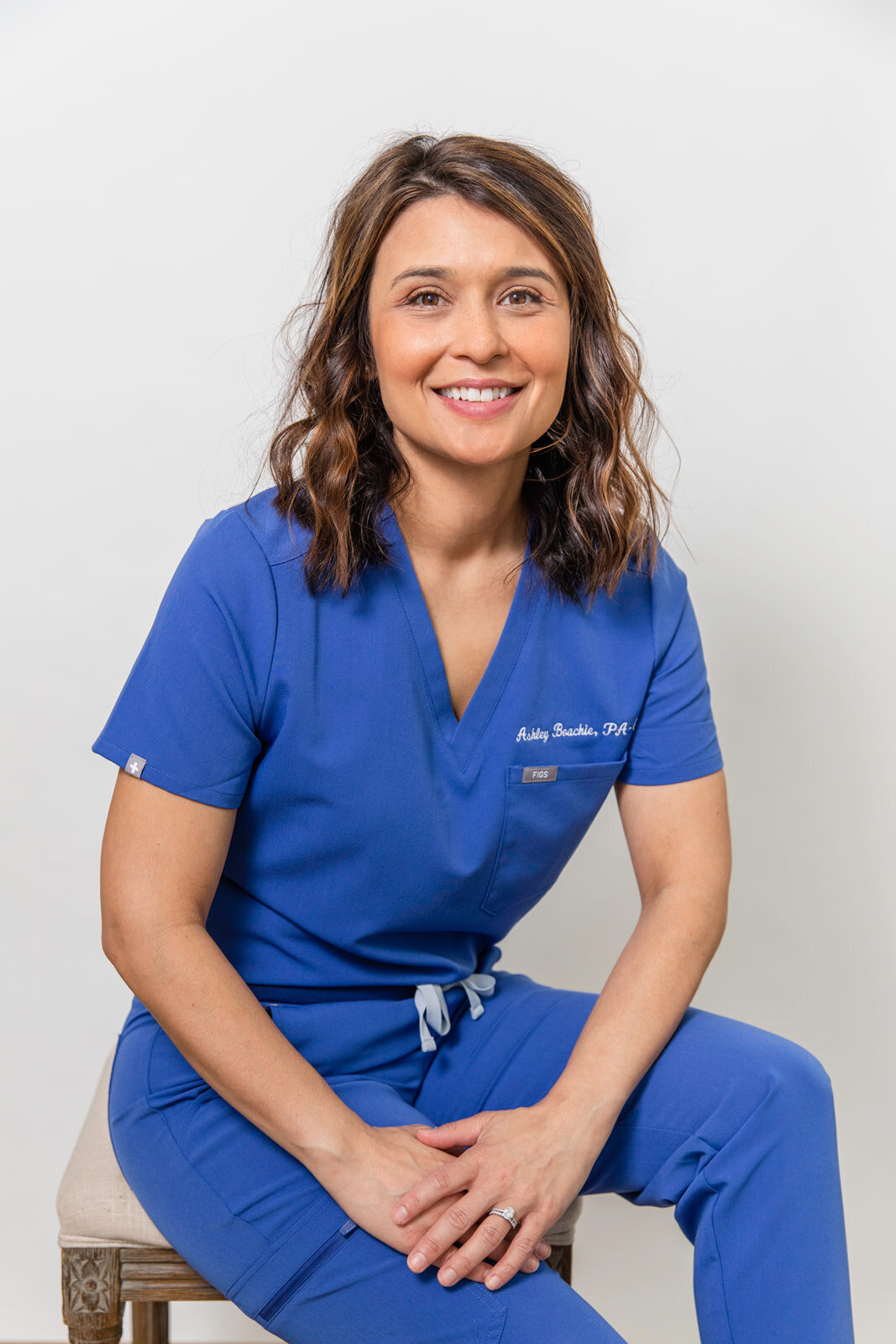 woman wearing doctor blue scrubs uniform sitting in front of grey background