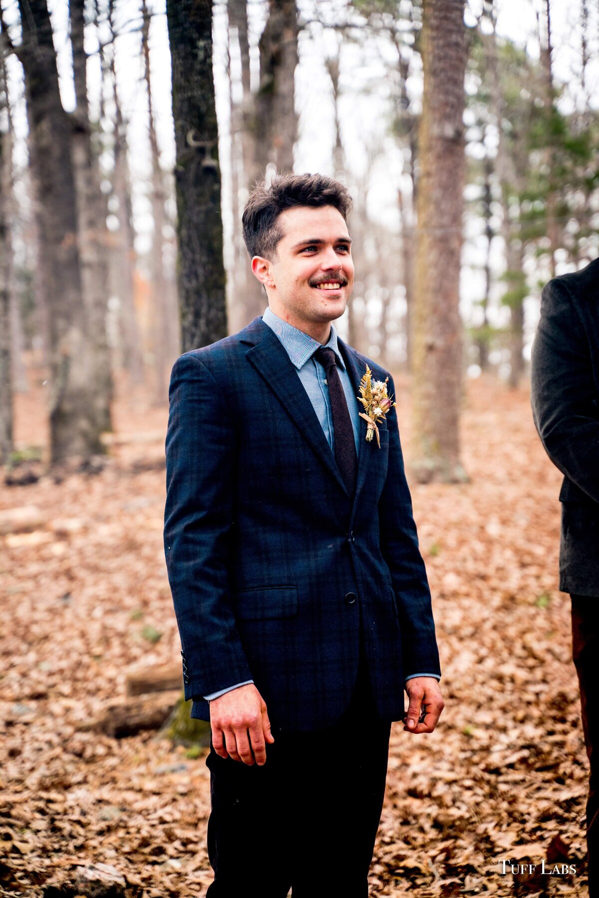 Groom smiles during outdoor wedding ceremony and wears a dried flowers boutonniere.