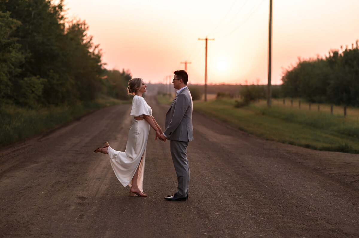 engaged couple dance on a dirt road at sunset