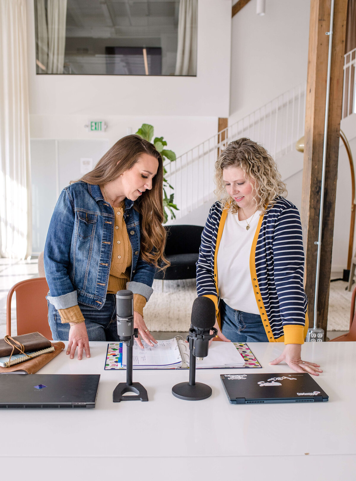 brand photography with two women  standing in front of their podcast technology and materials talking with one another for their brand photoshoot