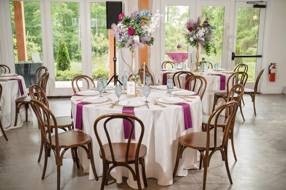 Elegant wedding reception decor featuring wooden chairs, floral centerpieces, and a natural backdrop.