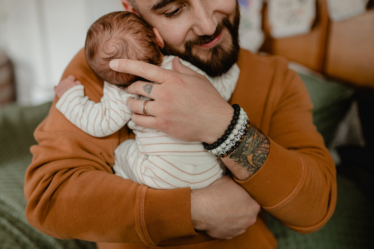 dad in an orange henley snuggling his newborn babyboy on his chest and over his shoulder