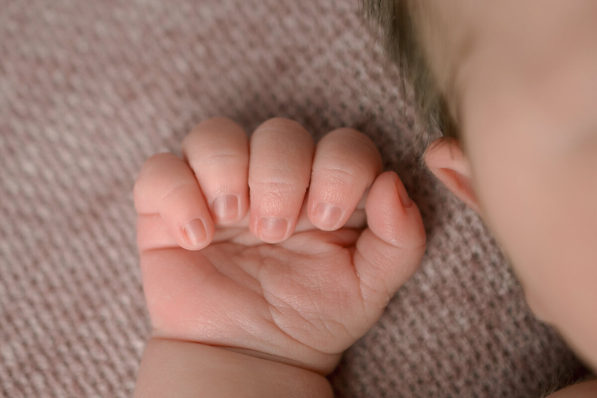 Details of a newborn's fist next to her ear