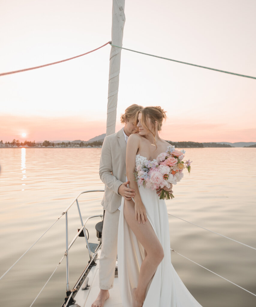 Intimate moment between bride and groom on the nose of a sailboat at sunset, captured by Ninth Avenue Studios. Featured on Bronte Bride.