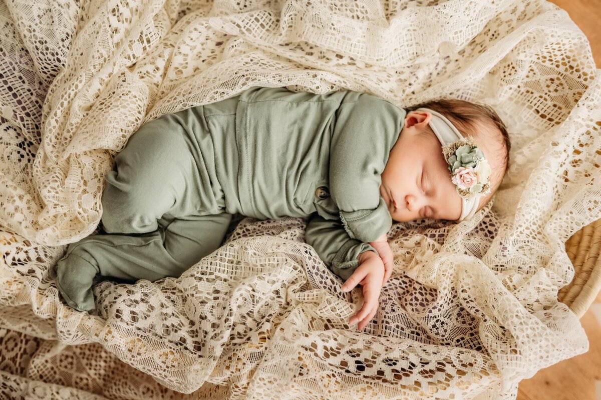 newborn baby girl in green sleeping on vintage lace