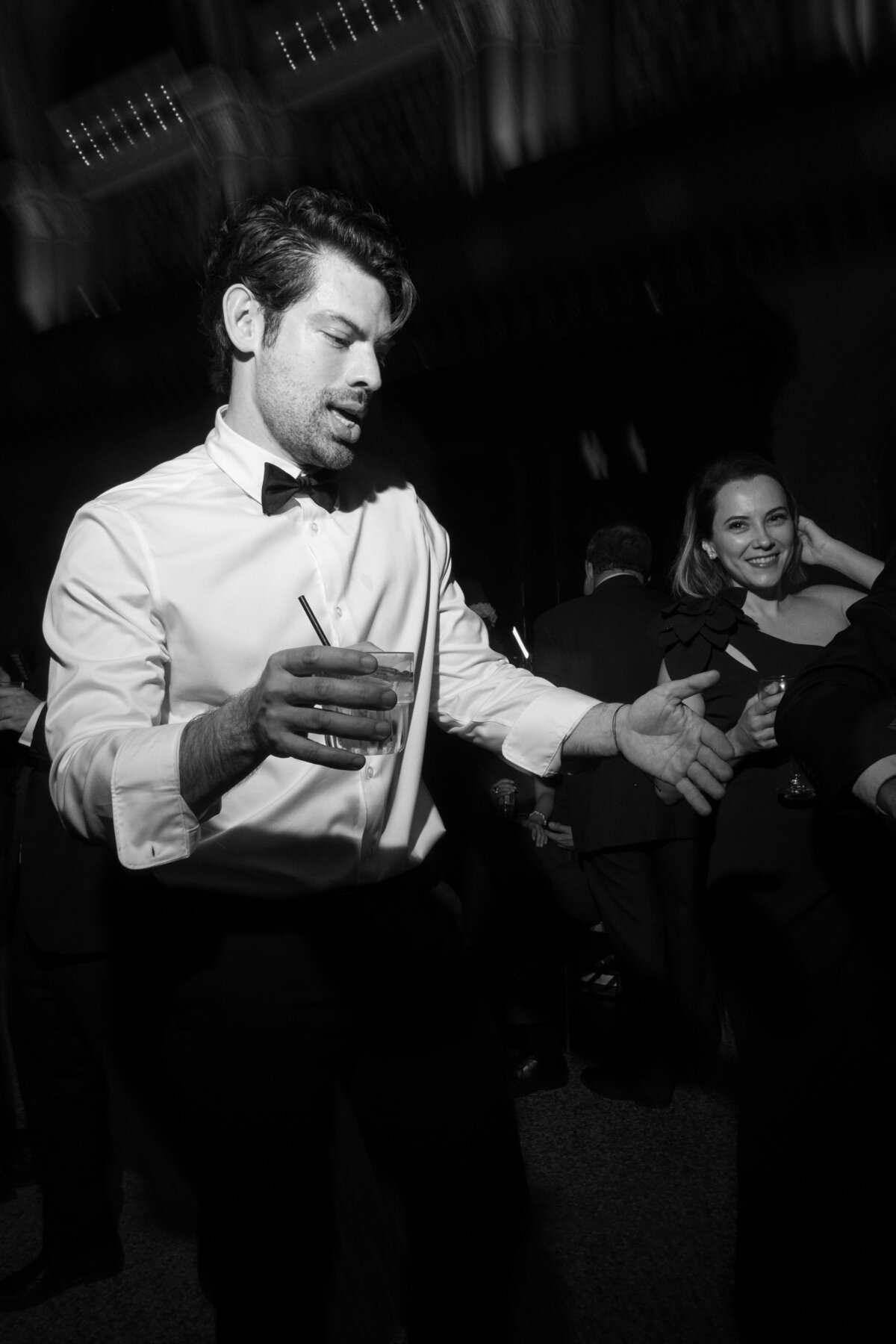 Black and white image of groom dancing with drink in hand at reception