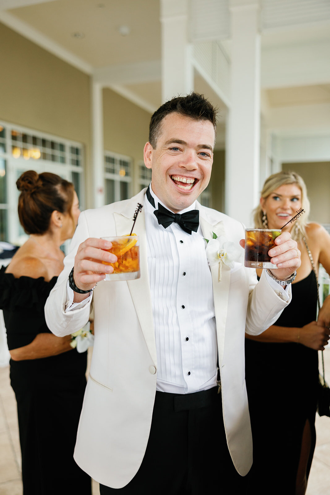 The groom cheerfully holding two drinks during Ashley and Cameron's micro wedding reception at Ocean Reef in Key Largo, captured by Claudia Amalia Photography.