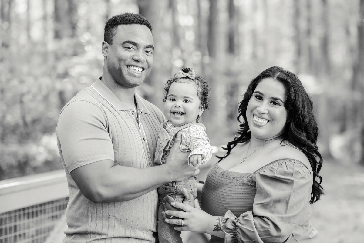 A young family including parents and a toddler smile wide for their fall family photos. The photo, taken in Chesapeake, is in black and white.