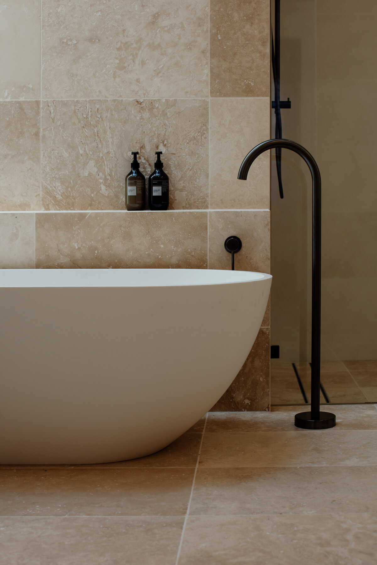 Minimalist bathroom designed by a Newcastle Kitchen and Bathroom Designer, featuring a freestanding bathtub and walk-in shower with beige tiles and black fixtures.