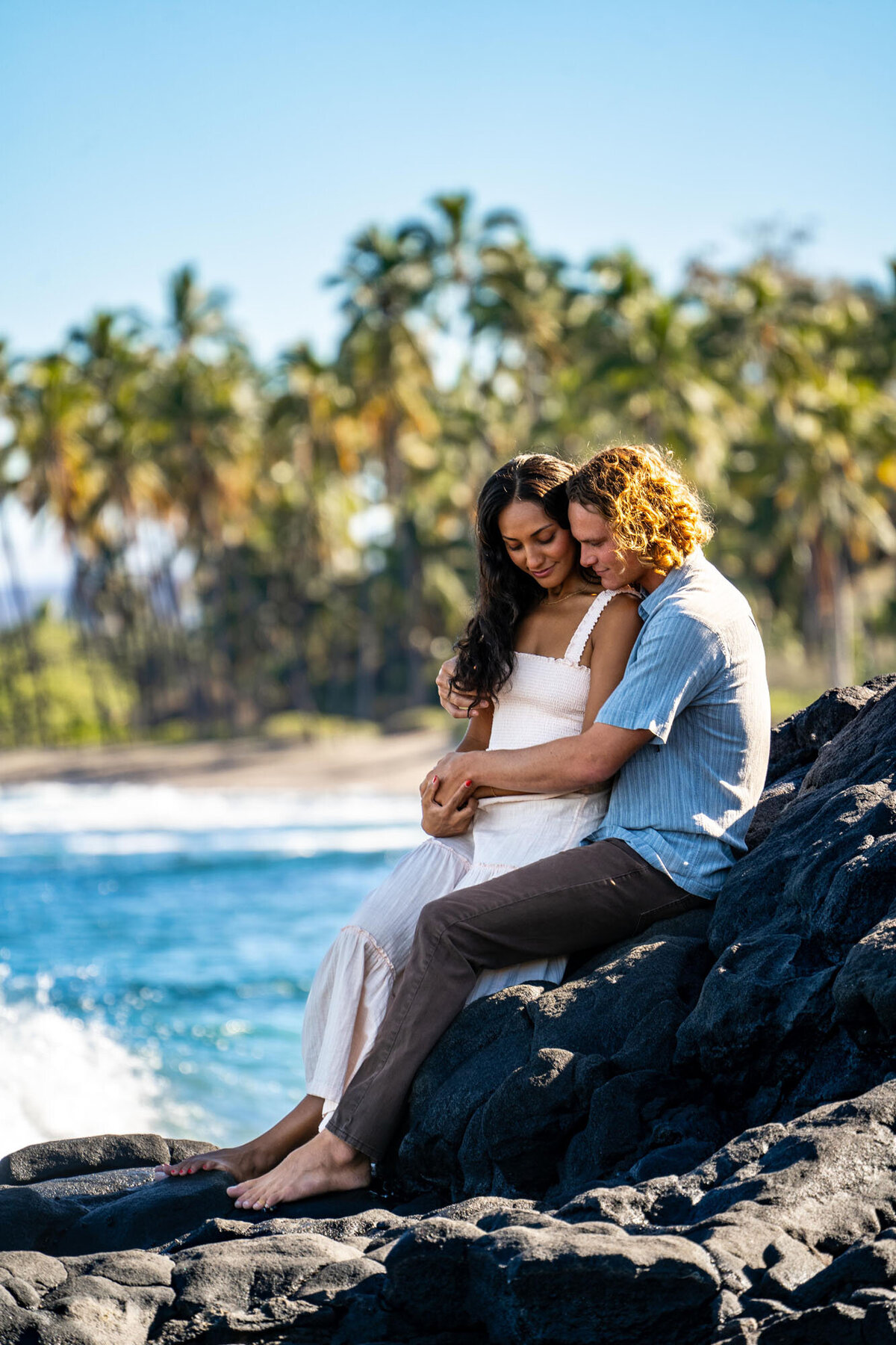 Couple sitting on lava rocks posing for engagement photographer in Hawaii
