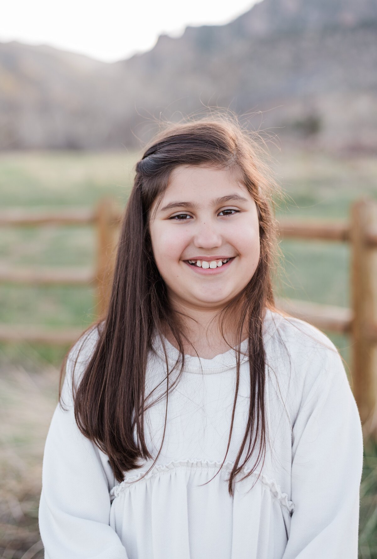 A young girl in a white long sleeve sweater smiles at the camera with boulder flat irons behind her