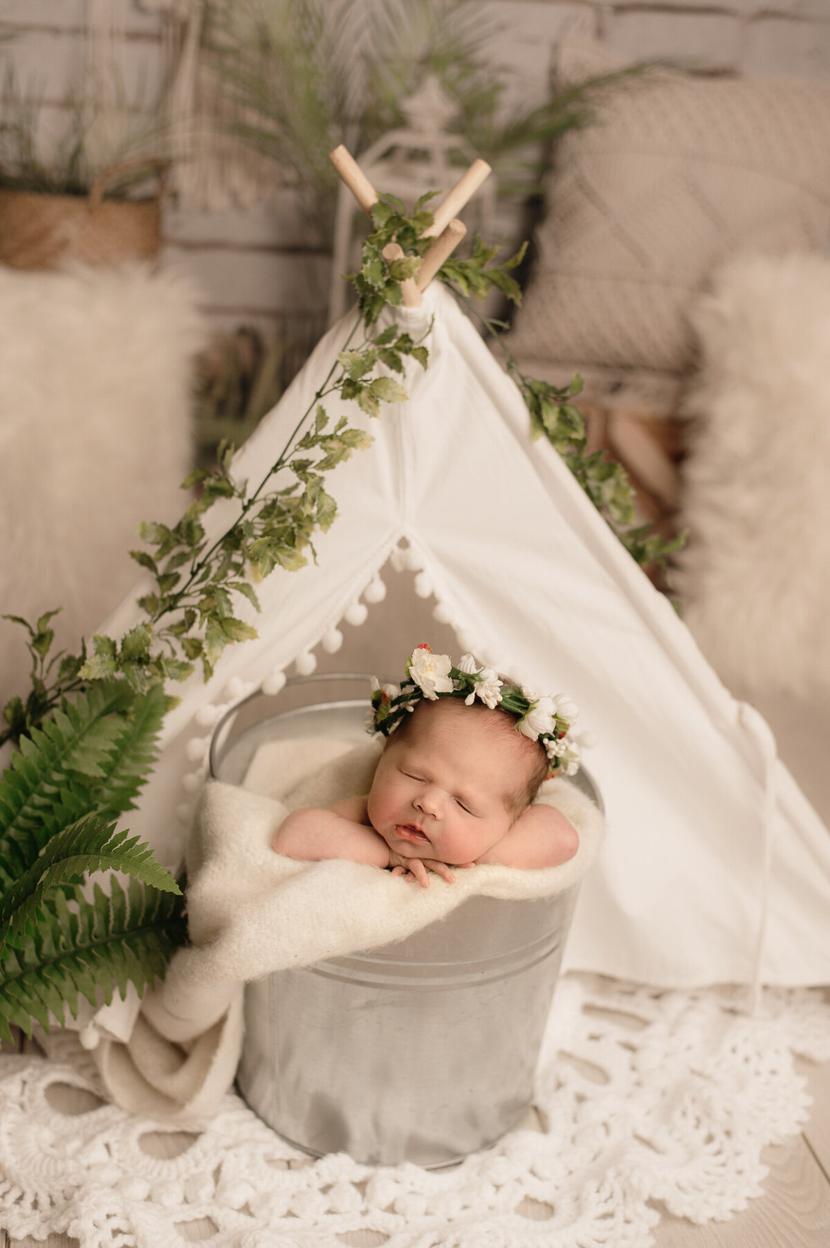 Baby girl in floral halo sleeping in a bucket in a teepee in studio.