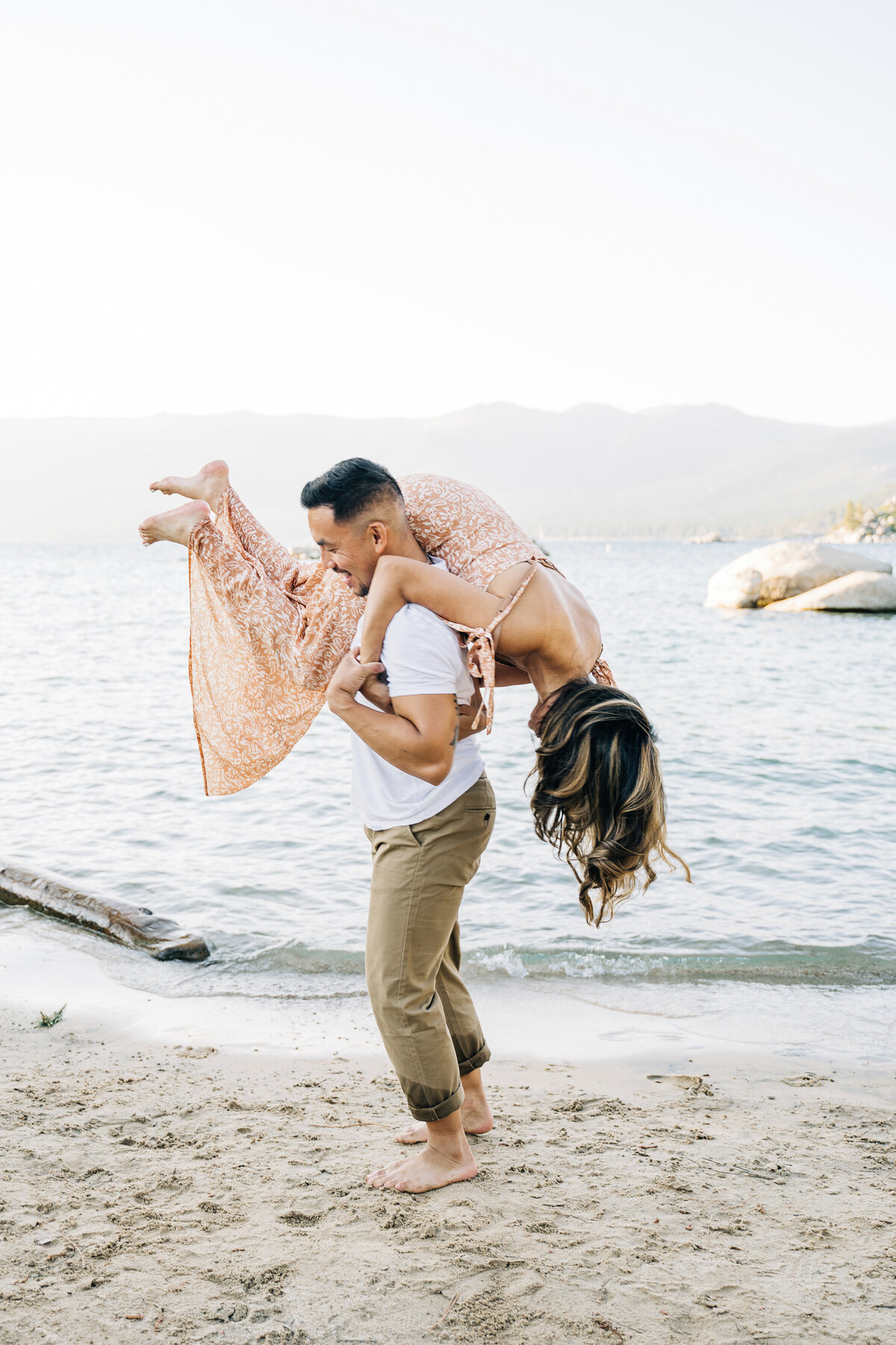 Man carries woman by lake in engagement shoot