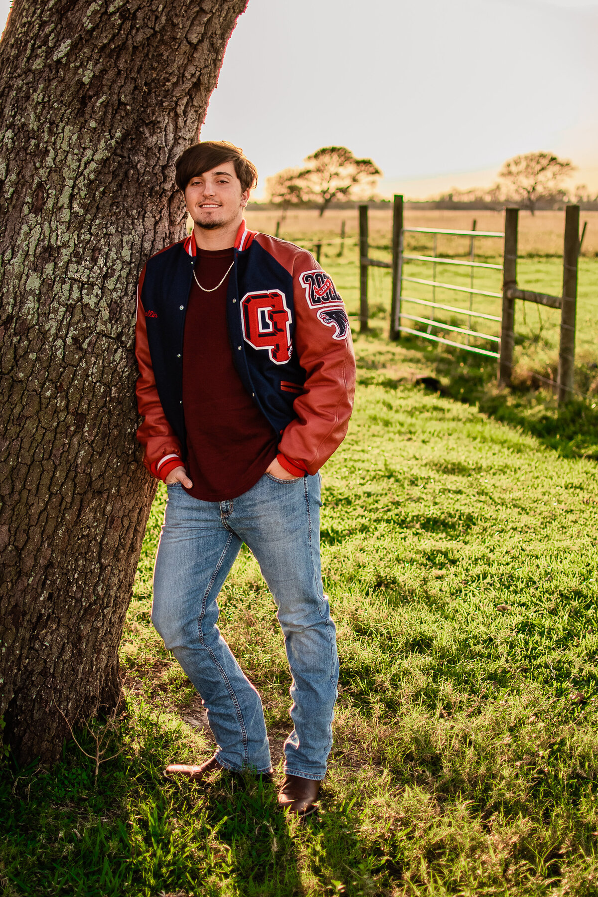 A Clear Lake High School senior leans against a tree at sunset.