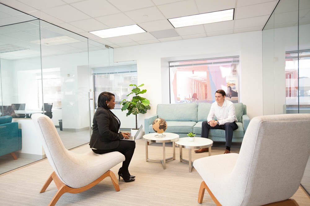 African-American woman sitting across from a young white male on modern furniture in the lobby of a commercial space