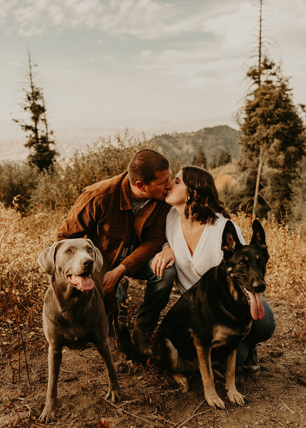 Couple kissing each other while holding their two dogs