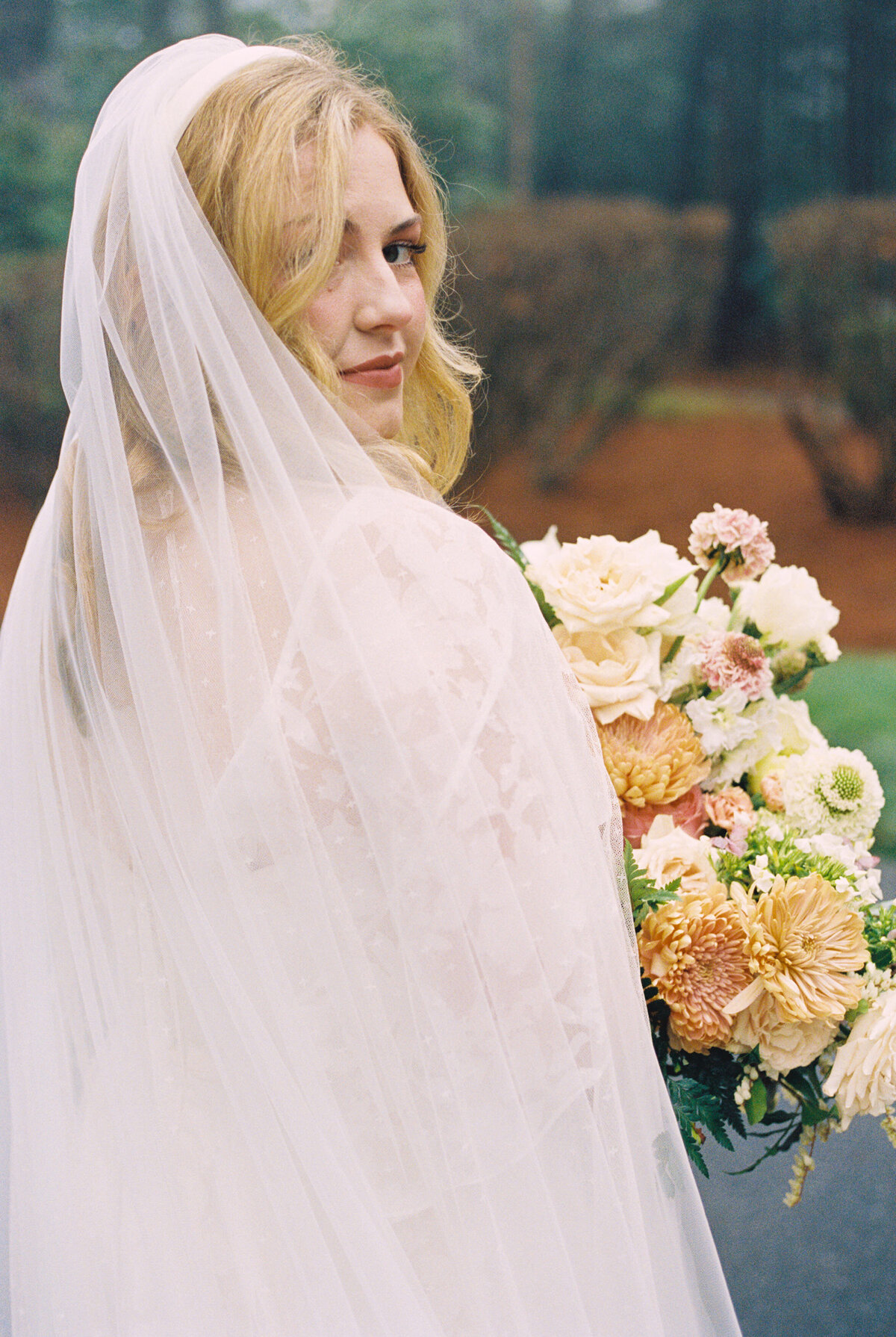 Bride wearing a veil and holding her wedding bouquet glances over her shoulder
