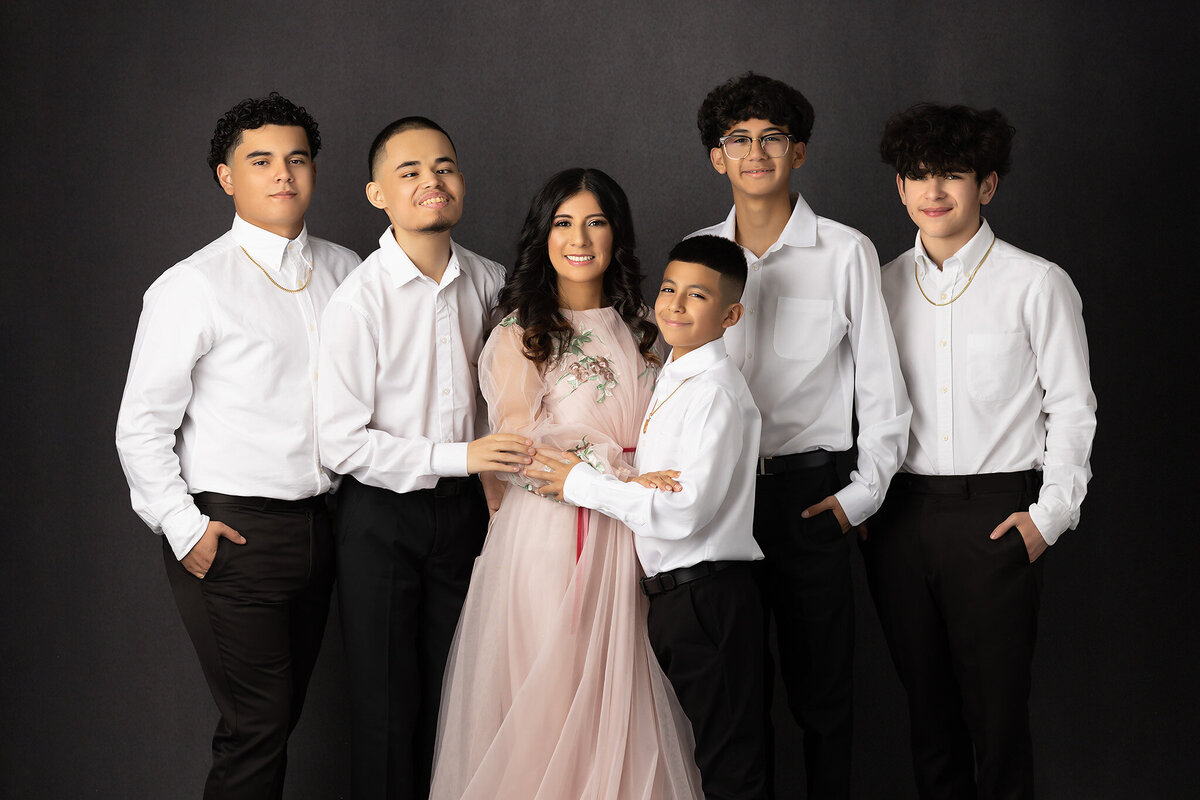 A Dallas family photographer captures a mother and her five children in a heartfelt family portrait, with everyone wearing coordinated white shirts against a dark backdrop.