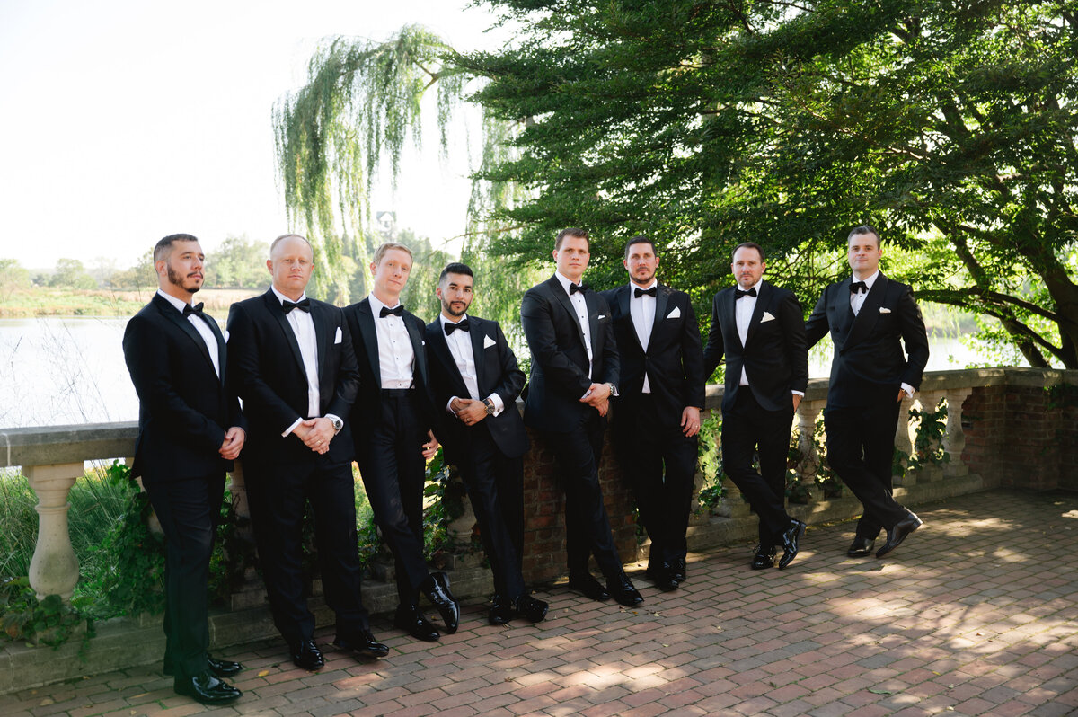 Groomsmen in black tuxedos lined up in a garden setting at the Chicago botanical gardens..