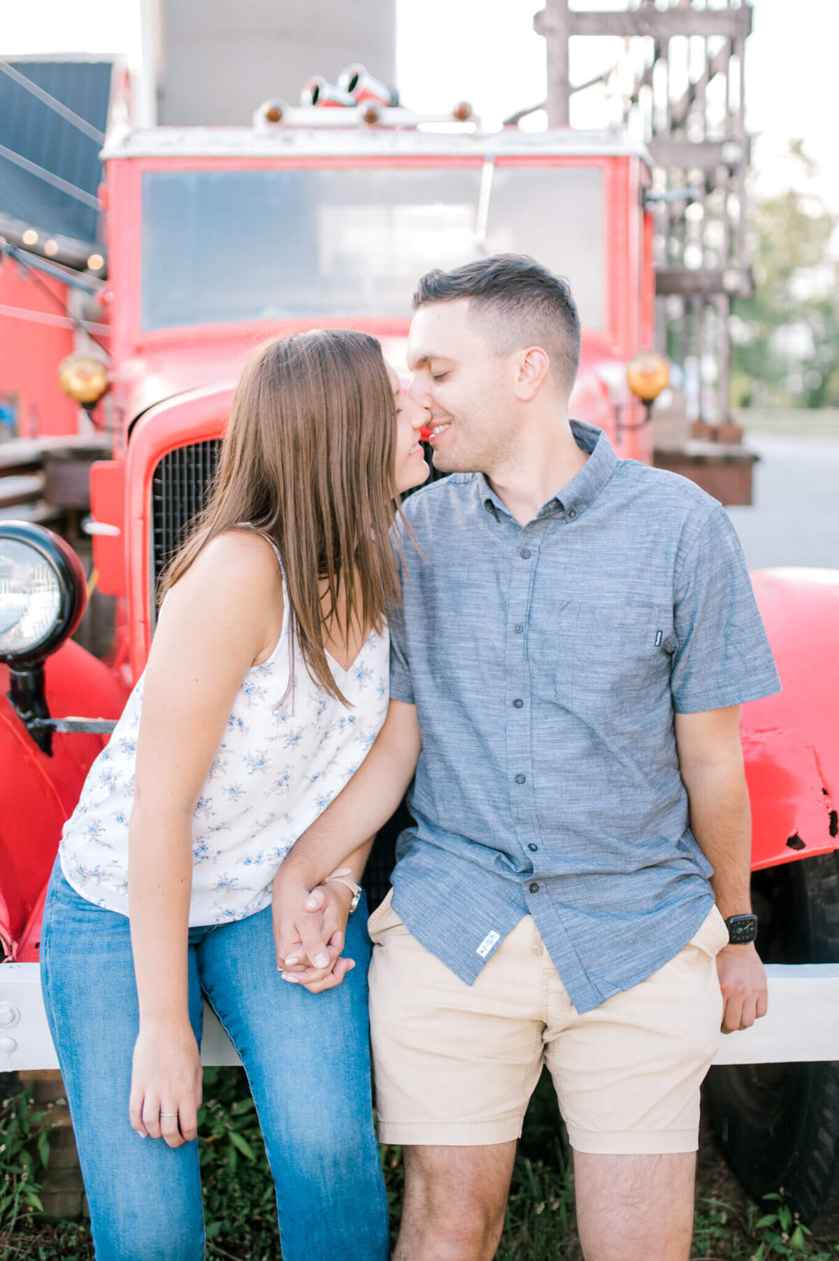 Niagara Wedding Photography. Engaged couple kissing while sitting at bumper of vintage fire truck