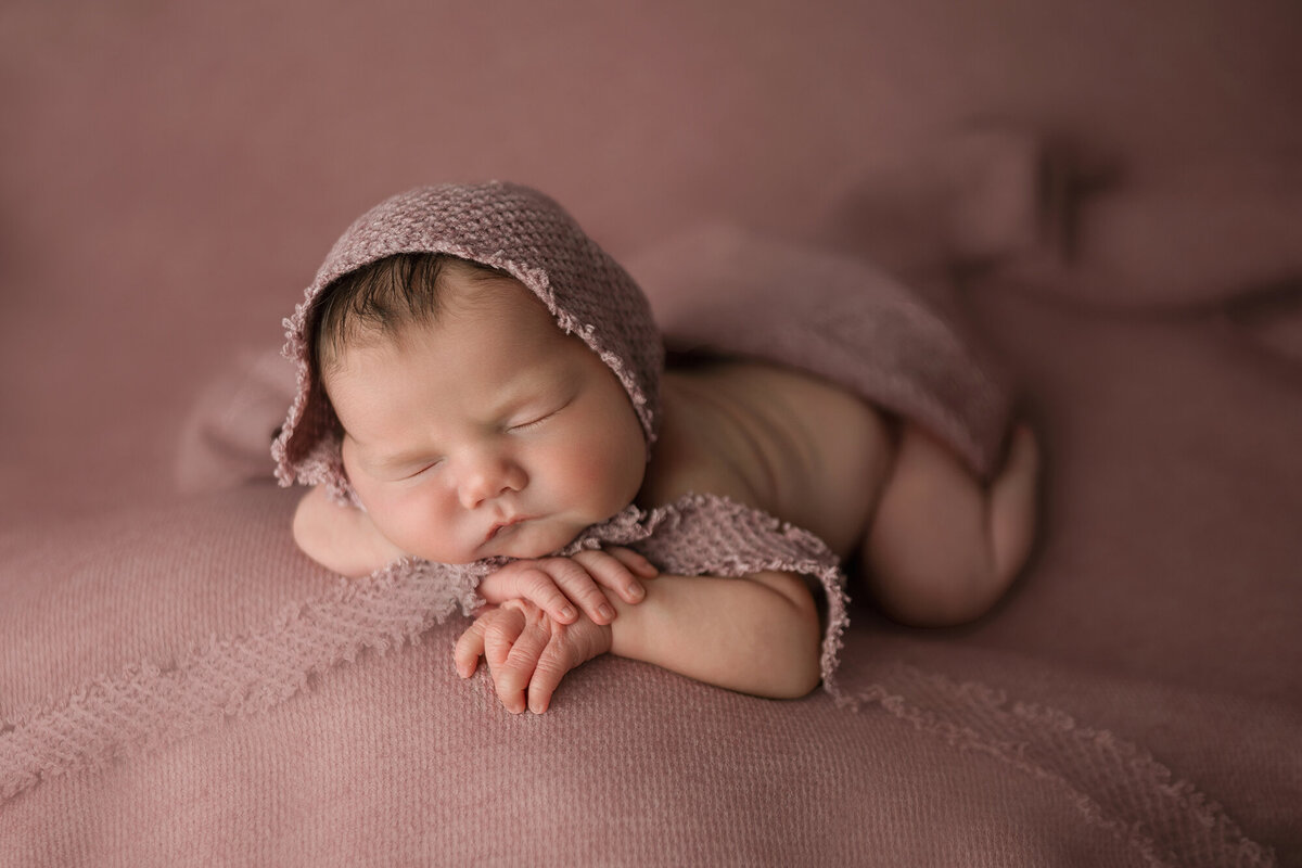 A newborn sleeps in a knit bonnet on matching bed