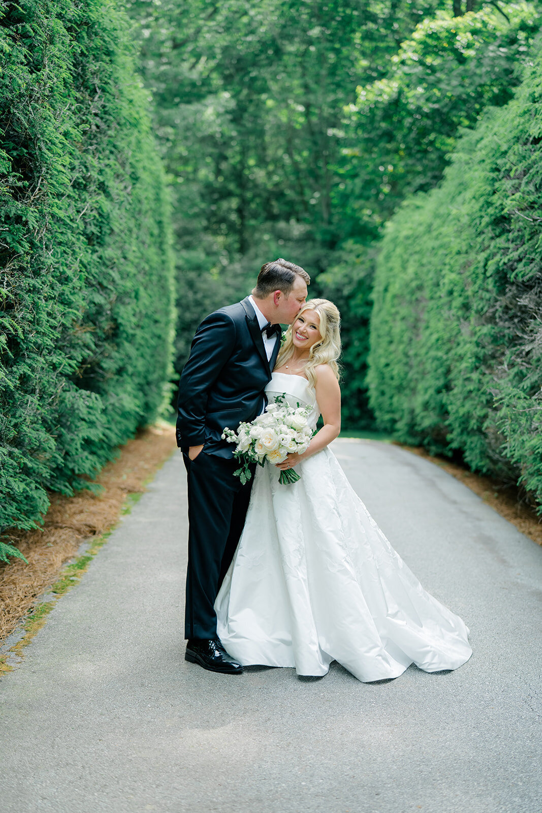  Bride and groom holding hands and walking down a tree-lined drive during their Highlands, NC wedding.