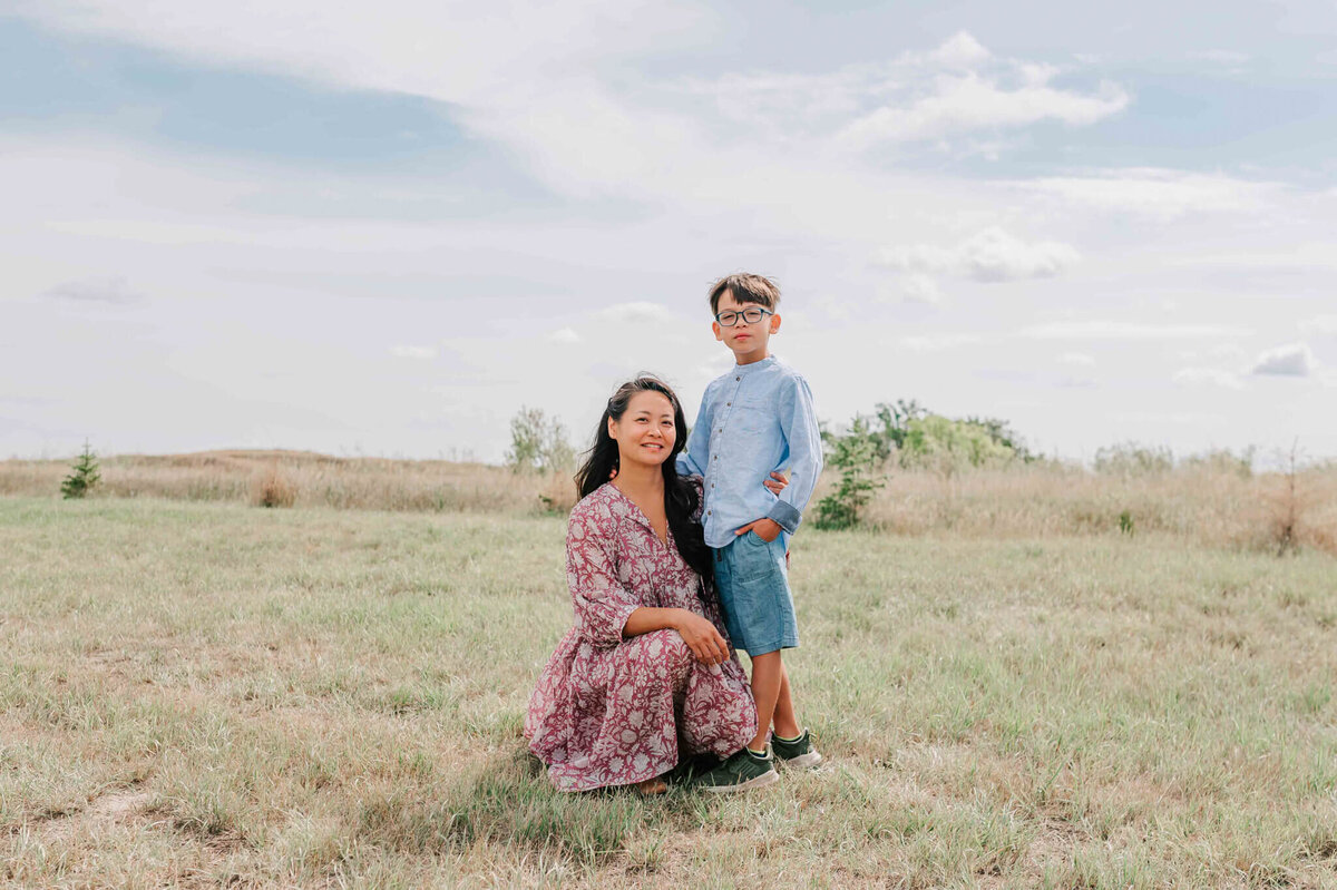 A mom crouching on the grass with her son standing next to her. 
