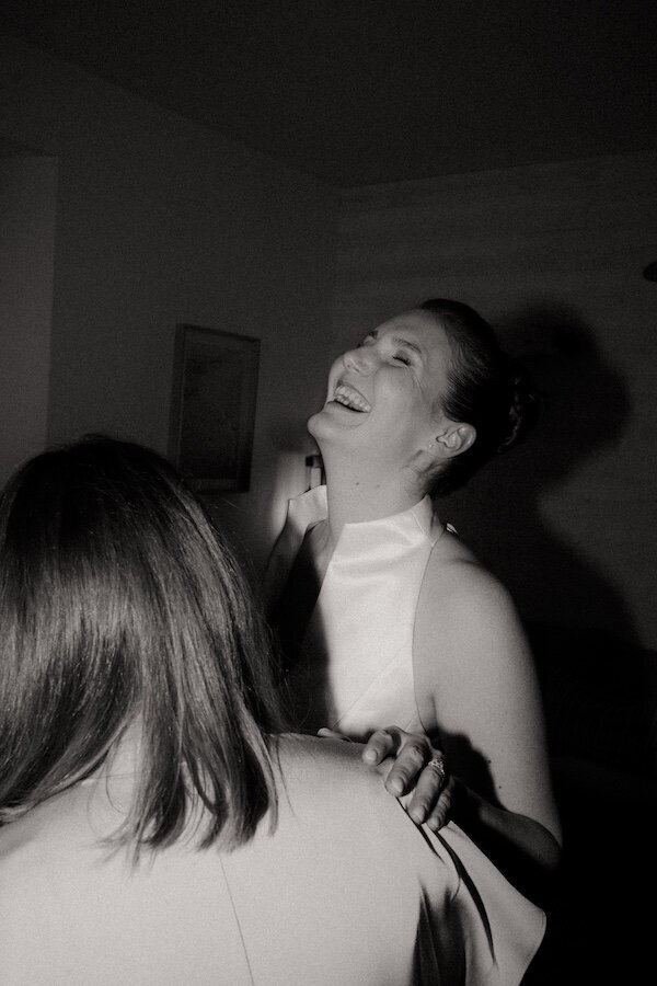 La mariée éclate de rire dans une ambiance intimiste et complice lors de la préparation. Photographie en noir et blanc par Kamescop.