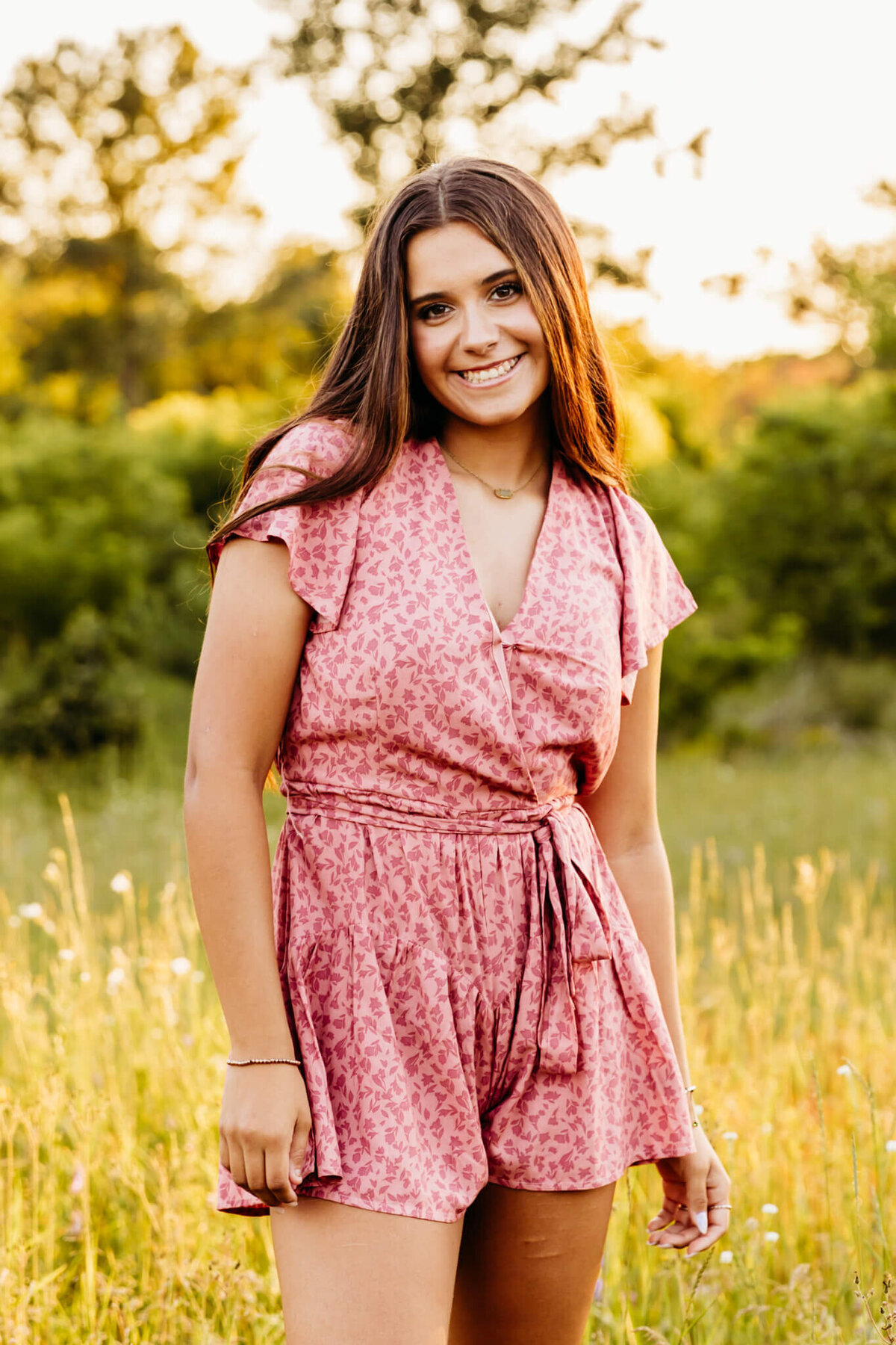 beautiful young woman from Oshkosh standing in a field at sunset for her summer senior photo session