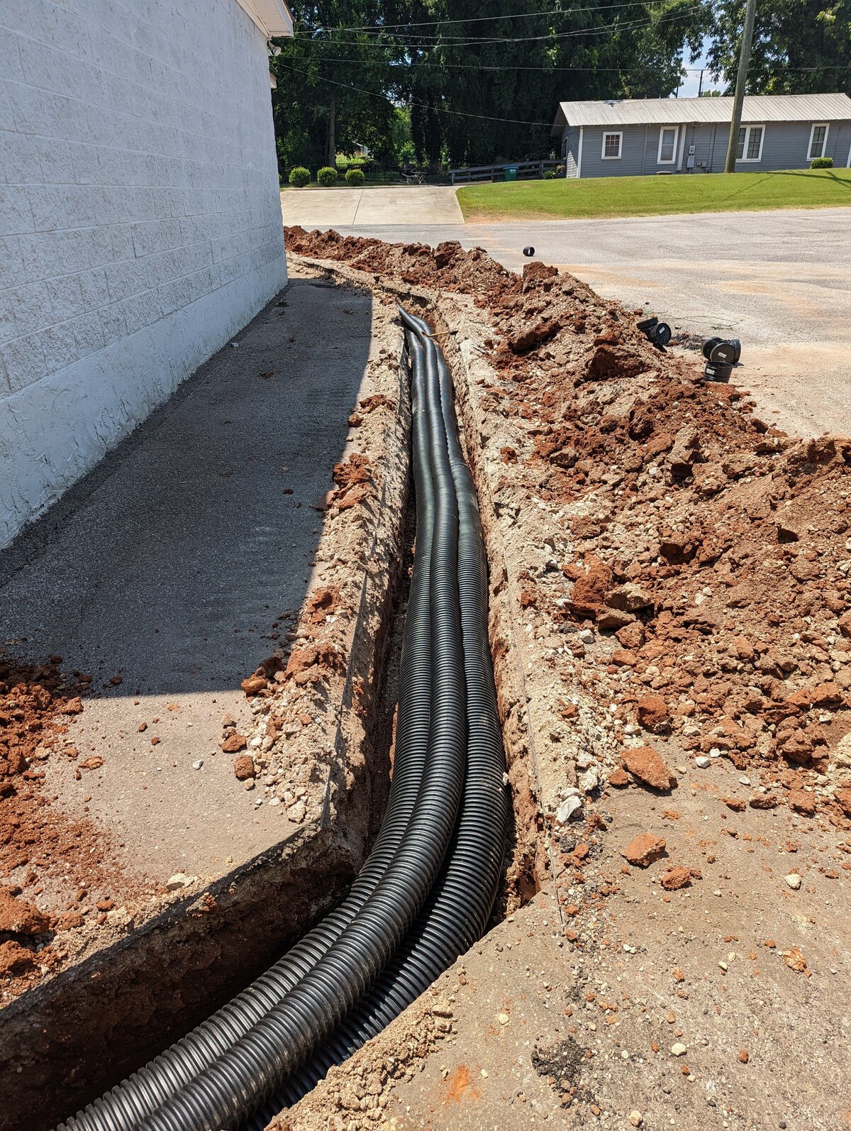 black-drainage-hoses-in-dirt-trench-next-to-white-brick-wall
