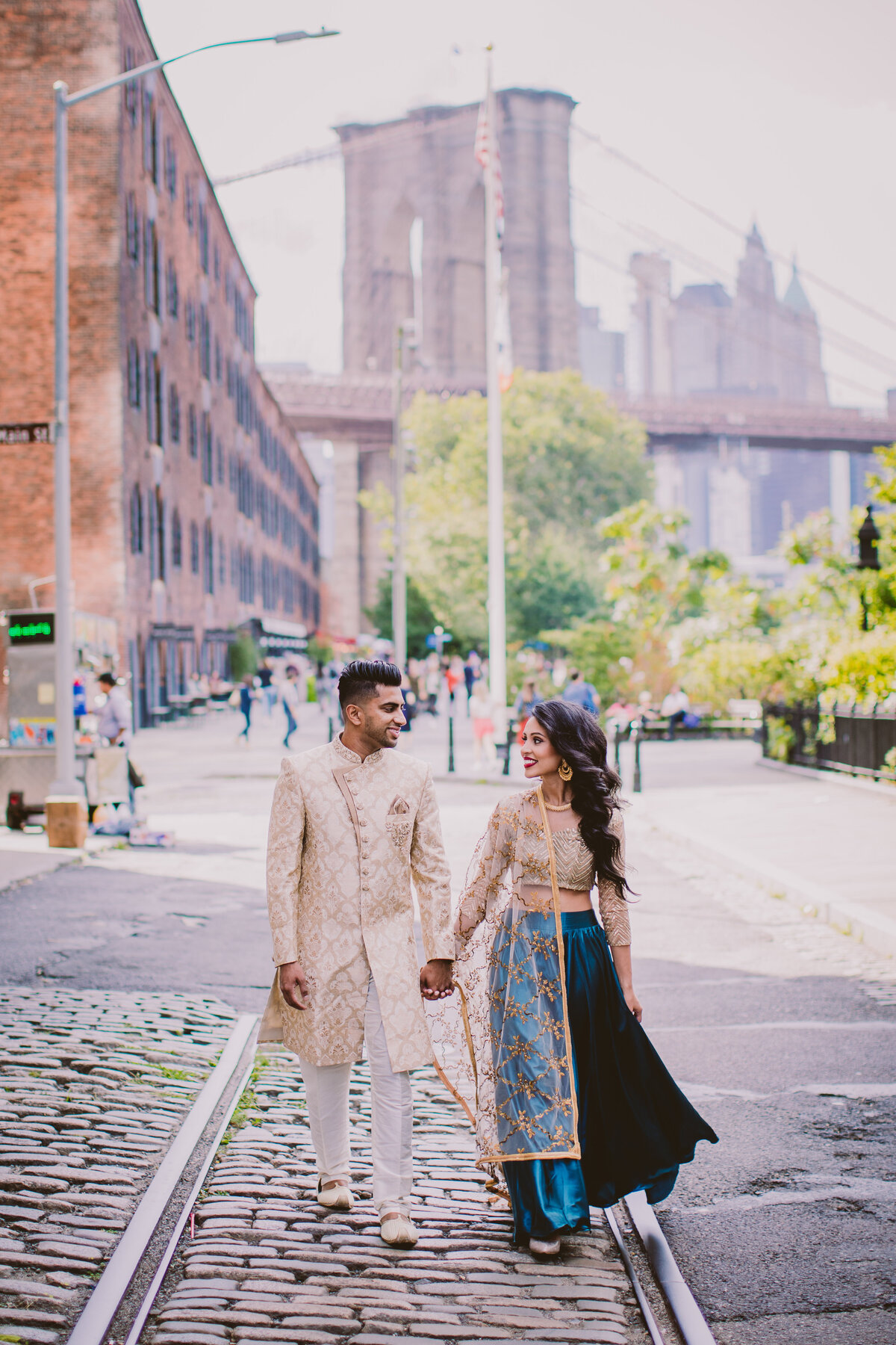 A couple in indian clothes during their engagement session walking on cobblestone plymouth street in the brooklyn bridge park in dumbo