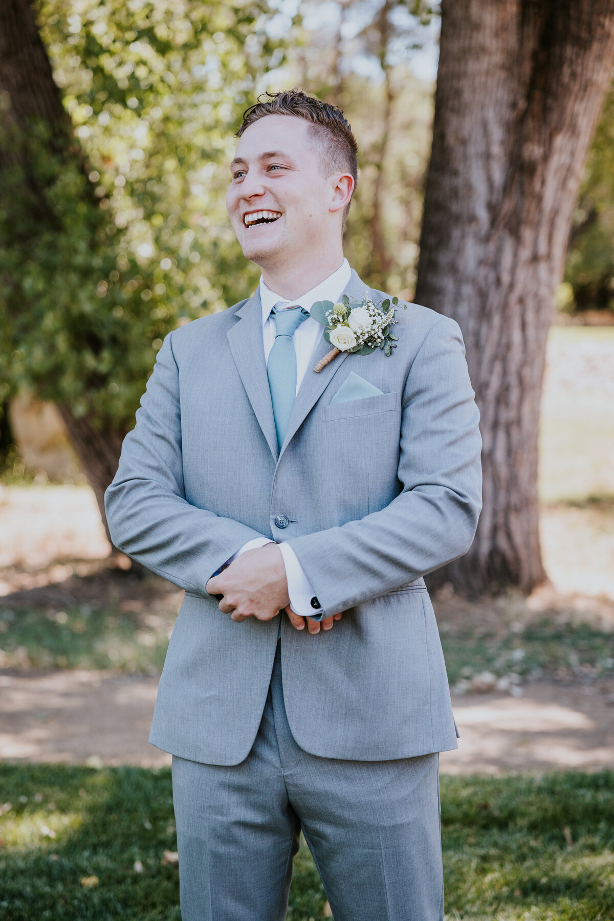 Groom adjusts sleeve while laughing at something just past the camera.