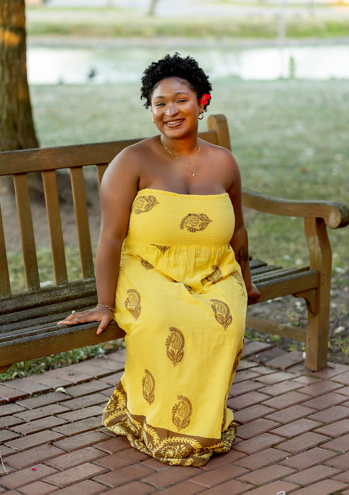 Woman in yellow halter sundress with red flower in her hair sitting on a bench in a park