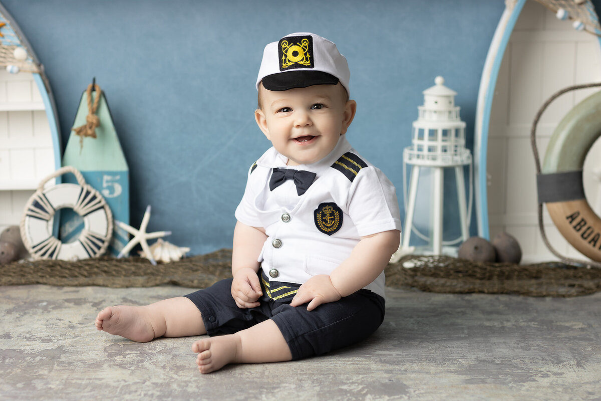 Baby boy dressed in a sailor outfit smiling during a nautical-themed milestone session with maritime props, captured by a DFW milestone photographer.