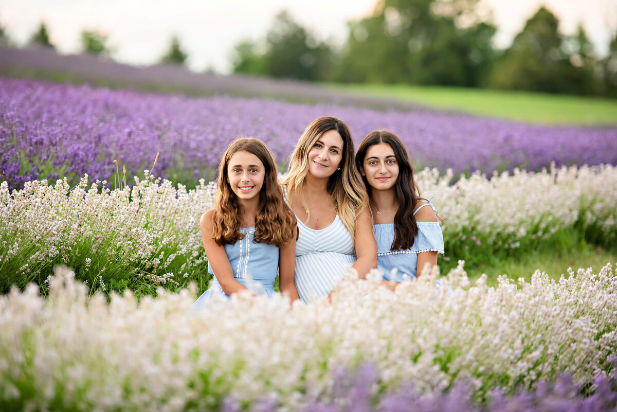Pregnant woman sitting on the ground with her twin daughters for her lavender maternity photography session in Burlington, On