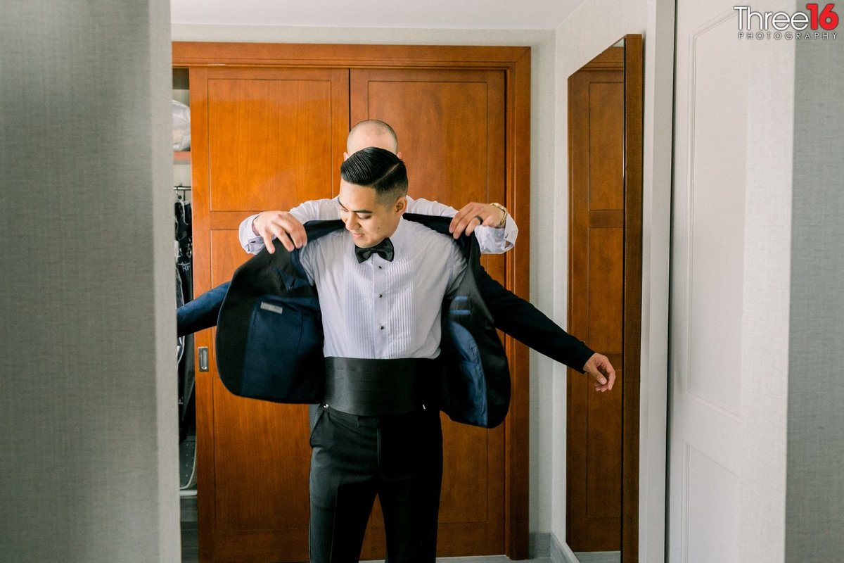 Groomsman assists with putting the Groom's tux coat on him