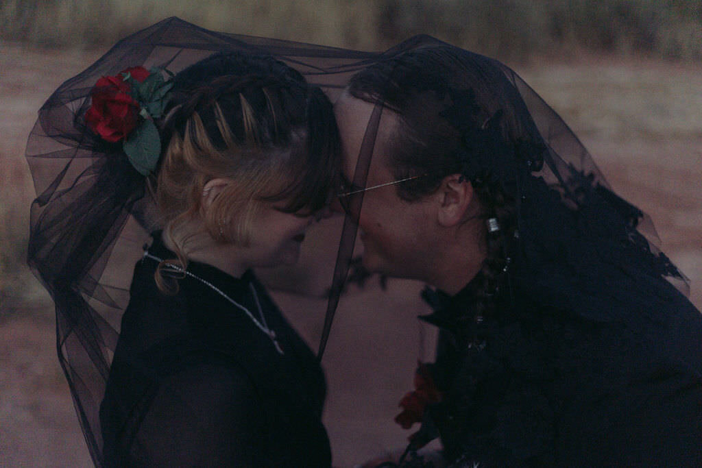 A newlywed couple about to kiss under a black veil.