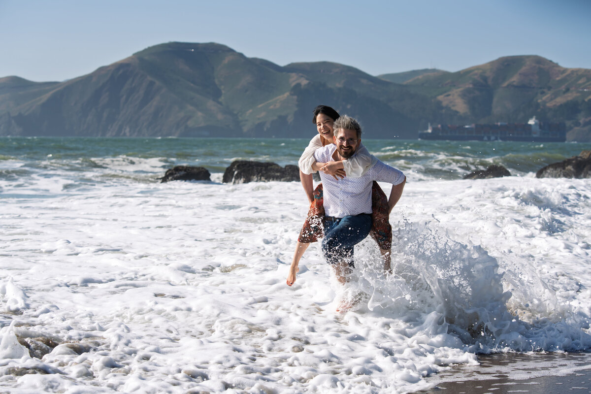 Man carrying woman through high surf at the beach.